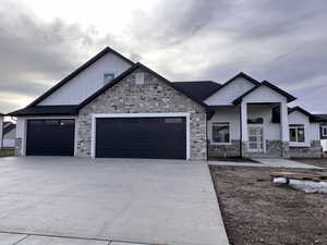 View of front of property featuring covered porch, board and batten siding, stone siding, and driveway