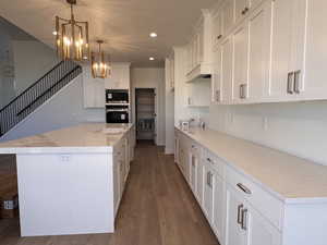 Kitchen with dark wood-style flooring, a chandelier, white cabinets, a center island, and recessed lighting