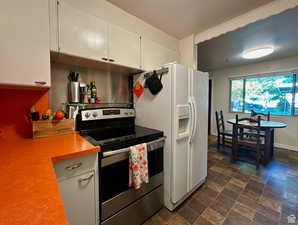 Kitchen with stainless steel range with electric cooktop, light countertops, stone finish flooring, white cabinetry, and white fridge with ice dispenser
