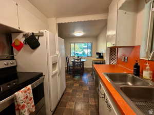 Kitchen with stainless steel electric range oven, white cabinets, stone finish flooring, and white refrigerator with ice dispenser