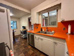 Kitchen with stainless steel appliances, backsplash, light countertops, and stone finish flooring