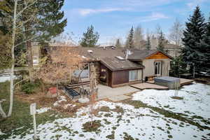 Snow covered property with a patio, a hot tub, stone siding, and roof with shingles