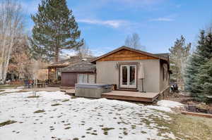 Snow covered rear of property featuring a hot tub, french doors, a patio area, and stucco siding