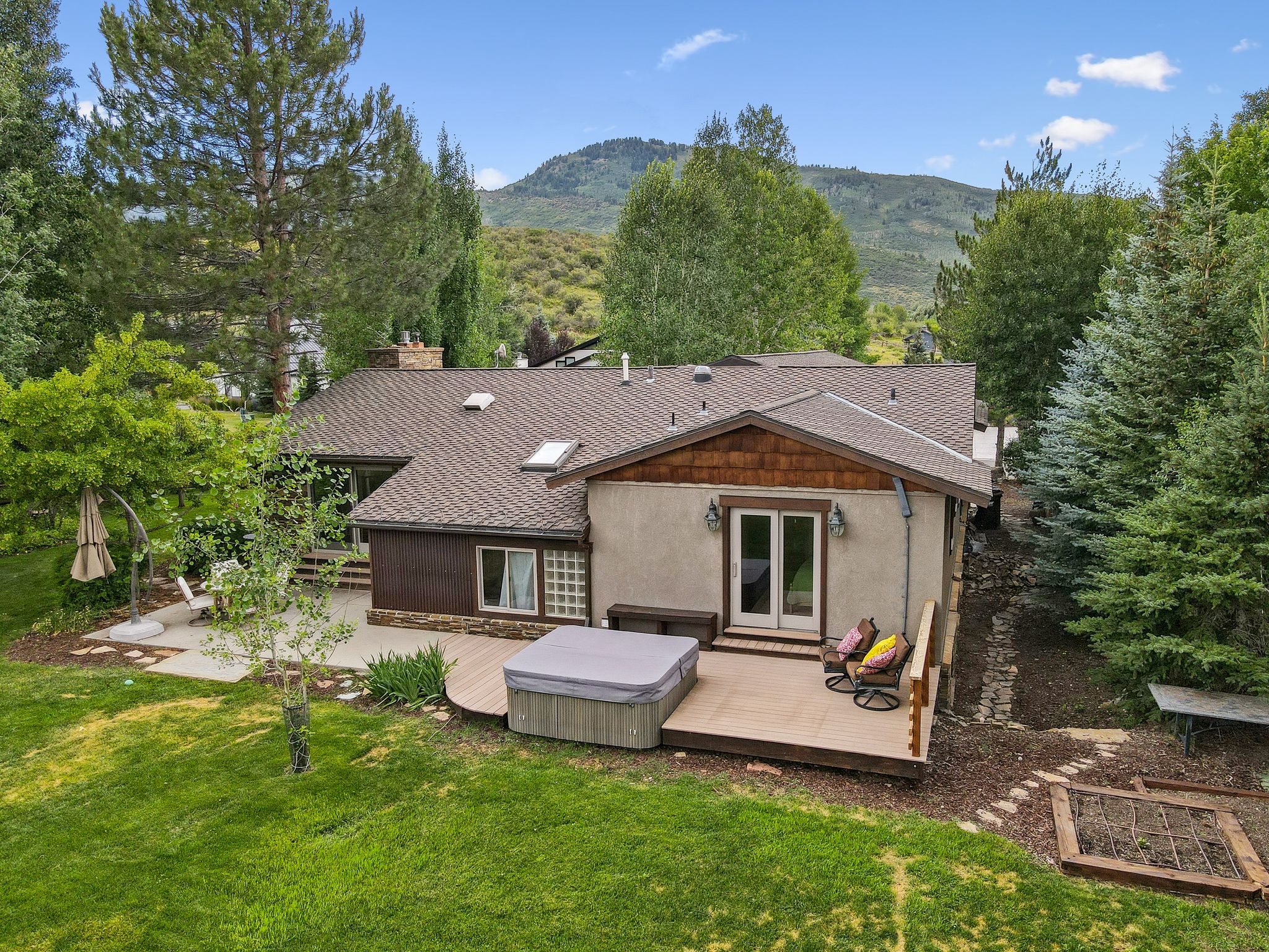 Rear view of house featuring a deck with mountain view, a yard, roof with shingles, stucco siding, and a chimney