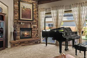 Sitting room with carpet floors, a stone fireplace, and beamed ceiling
