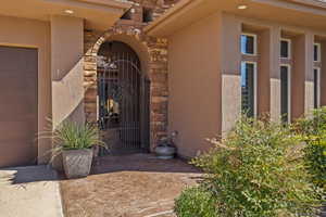 Doorway to property featuring stone siding, stucco siding, and a gate