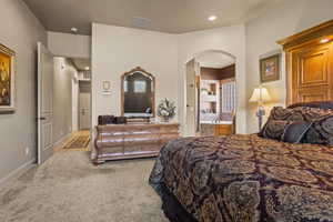 Bedroom with arched walkways, light colored carpet, recessed lighting, and ensuite bath