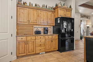 Kitchen featuring black appliances, light stone countertops, backsplash, brown cabinets, and light tile patterned flooring