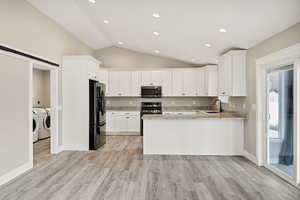 Kitchen with a barn door, light stone counters, vaulted ceiling, white cabinetry, and stainless steel appliances