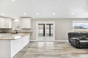 Kitchen featuring light stone countertops, recessed lighting, white cabinets, light wood-style floors, and a peninsula