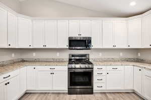 Kitchen featuring appliances with stainless steel finishes, white cabinetry, and vaulted ceiling