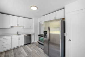 Kitchen featuring stainless steel appliances, a textured ceiling, white cabinetry, and light wood finished floors