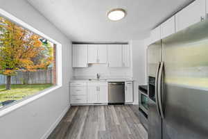Kitchen featuring stainless steel appliances, white cabinetry, light countertops, a textured ceiling, and light wood finished floors