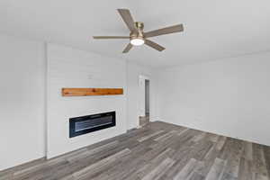 Unfurnished living room with a large fireplace, wood finished floors, ceiling fan, and a textured ceiling