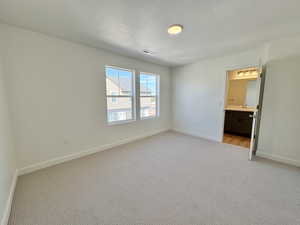 Unfurnished bedroom featuring light colored carpet, a textured ceiling, and ensuite bath