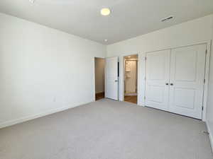Unfurnished bedroom with ensuite bath, carpet flooring, a closet, and a textured ceiling