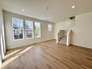 Unfurnished living room with stairs, light wood finished floors, recessed lighting, and a textured ceiling