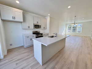 Kitchen with stainless steel appliances, open floor plan, white cabinetry, hanging light fixtures, and an island with sink