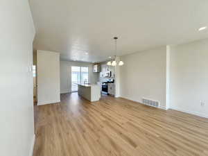 Unfurnished living room featuring light wood-style flooring, a chandelier, a textured ceiling, and recessed lighting