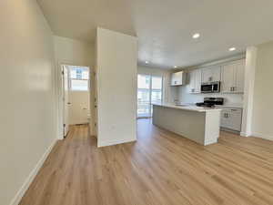 Kitchen featuring a center island with sink, stainless steel appliances, recessed lighting, light wood-type flooring, and light stone counters