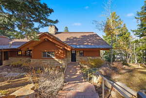 Rustic home with a chimney, stone siding, and roof with shingles