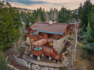Back of house at dusk featuring a wooden deck, stone siding, a chimney, and a metal roof