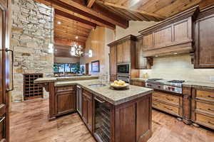 Kitchen featuring high vaulted ceiling, a chandelier, decorative light fixtures, an island with sink, and light wood-style flooring