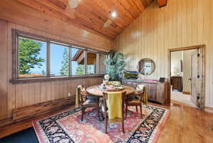 Dining room with wooden walls, high vaulted ceiling, light wood-type flooring, and wooden ceiling