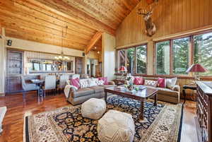 Living room featuring high vaulted ceiling, wooden walls, wood finished floors, a chandelier, and a wooden ceiling with exposed beams