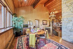 Dining area with baseboard heating, wood finished floors, wood walls, a wood ceiling with exposed beams, and high vaulted ceiling