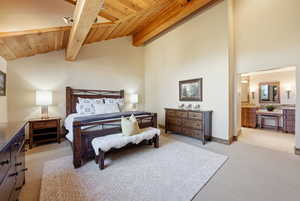 Bedroom with light colored carpet, a wooden ceiling with exposed beams, a ceiling fan, high vaulted ceiling, and ensuite bath