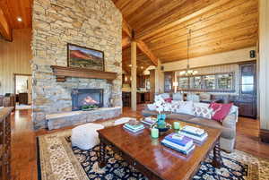 Living area with high vaulted ceiling, hardwood / wood-style flooring, wood walls, a fireplace, and a chandelier