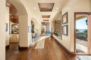 Corridor featuring dark wood-type flooring, arched walkways, a tray ceiling, and recessed lighting
