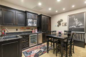 Kitchen featuring dark stone counters, dark brown cabinets, beverage cooler, stainless steel microwave, and recessed lighting