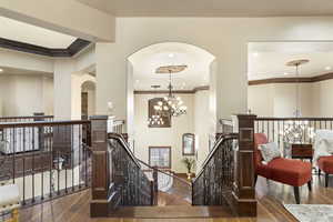 Corridor featuring an upstairs landing, arched walkways, a chandelier, dark wood finished floors, and crown molding