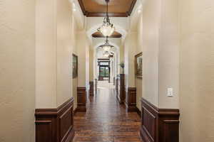Hallway with a textured wall, arched walkways, crown molding, wainscoting, and dark wood-style flooring