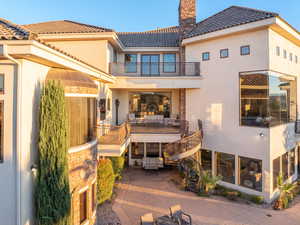 Rear view of property featuring a balcony, stucco siding, a tiled roof, a chimney, and stairs