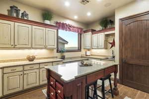 Kitchen featuring dark wood finished floors, light stone countertops, a breakfast bar, a center island, and recessed lighting