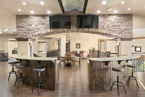 Indoor bar featuring recessed lighting, light stone countertops, dark wood-type flooring, vaulted ceiling, and arched walkways