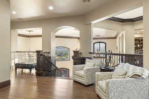 Living area with a chandelier, wood finished floors, ornamental molding, recessed lighting, and arched walkways