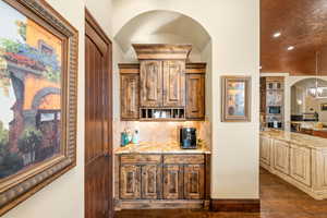 Bar area featuring arched walkways, light stone countertops, backsplash, recessed lighting, and appliances with stainless steel finishes