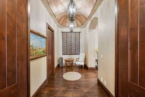 Corridor featuring a chandelier, dark wood-style flooring, arched walkways, and lofted ceiling