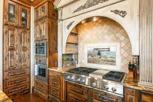 Kitchen featuring backsplash, light stone countertops, stainless steel gas stovetop, exhaust hood, and brown cabinets