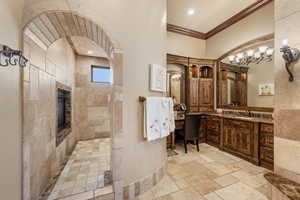 Bathroom featuring vanity, stone tile flooring, walk in shower, and crown molding
