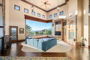 Living room featuring a high ceiling, a fireplace with raised hearth, crown molding, ceiling fan, and wood-type flooring