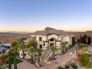 View of front facade featuring stucco siding, stairs, driveway, a chimney, and a balcony