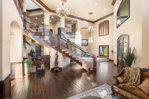 Living area featuring ornamental molding, arched walkways, dark wood-style flooring, a chandelier, and a high ceiling
