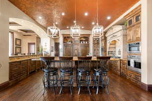 Kitchen featuring recessed lighting, lofted ceiling, hanging light fixtures, a kitchen bar, and light stone countertops