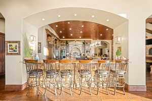 Bar featuring arched walkways, hanging light fixtures, recessed lighting, dark stone counters, and light wood-type flooring