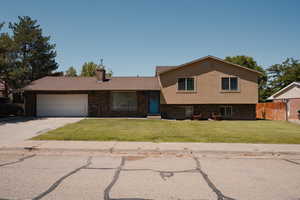 Split level home featuring driveway, a chimney, brick and stucco siding, and a garage